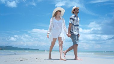 Genç çift beyaz kumlu sahilde tatil yapıyor, açık gökyüzü ve deniz.