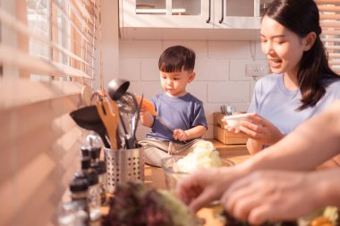 Mutlu Asyalı ebeveynler, yeni yürümeye başlayan çocuklarıyla mutfakta yemek yerken, beslenme saatlerinde kahkahalarını ve neşeli anlarını paylaşıyorlar.