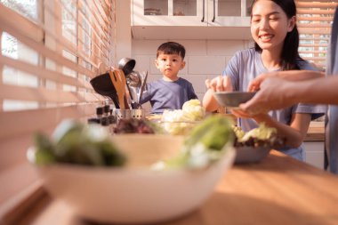 Mutlu Asyalı ebeveynler, yeni yürümeye başlayan çocuklarıyla mutfakta yemek yerken, beslenme saatlerinde kahkahalarını ve neşeli anlarını paylaşıyorlar.