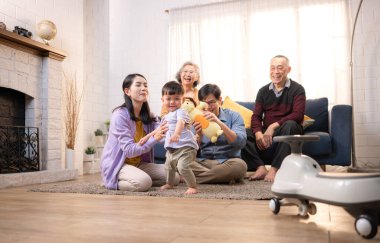 Mutlu çoklu Asyalı bir aile evde keyifle vakit geçiriyor, oyuncak bir arabayla rahat bir oturma odasında gülümsüyor ve gülümsüyor.