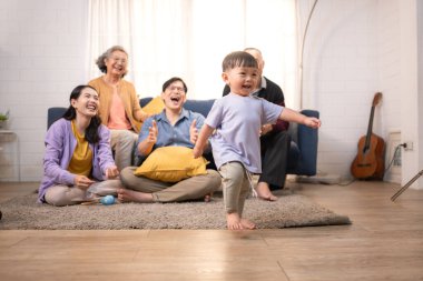 Mutlu çoklu Asyalı aile evde birlikte eğleniyor, bir bebekle tezahürat yapıyor ve gülümsüyor.