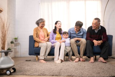 Mutlu çoklu Asyalı bir aile evde keyifle vakit geçiriyor, oyuncak bir arabayla rahat bir oturma odasında gülümsüyor ve gülümsüyor.