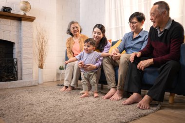 Mutlu çoklu Asyalı aile evde birlikte eğleniyor, bir bebekle tezahürat yapıyor ve gülümsüyor.
