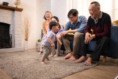 Mutlu çoklu Asyalı aile evde birlikte eğleniyor, bir bebekle tezahürat yapıyor ve gülümsüyor.