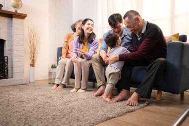 Mutlu çoklu Asyalı aile evde birlikte eğleniyor, bir bebekle tezahürat yapıyor ve gülümsüyor.