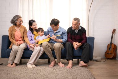 Mutlu çoklu Asyalı aile evde birlikte eğleniyor, bir bebekle tezahürat yapıyor ve gülümsüyor.