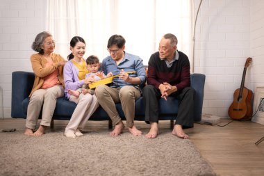 Mutlu çoklu Asyalı aile evde birlikte eğleniyor, bir bebekle tezahürat yapıyor ve gülümsüyor.
