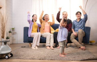 Mutlu çoklu Asyalı aile evde birlikte eğleniyor, bir bebekle tezahürat yapıyor ve gülümsüyor.