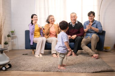 Mutlu çoklu Asyalı aile evde birlikte eğleniyor, bir bebekle tezahürat yapıyor ve gülümsüyor.