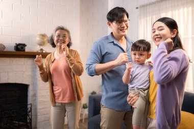 Mutlu çoklu Asyalı aile evde birlikte eğleniyor, bir bebekle tezahürat yapıyor ve gülümsüyor.