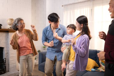 Mutlu çoklu Asyalı aile evde birlikte eğleniyor, bir bebekle tezahürat yapıyor ve gülümsüyor.