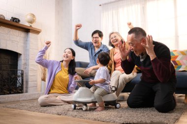 Mutlu çoklu Asyalı bir aile evde keyifle vakit geçiriyor, oyuncak bir arabayla rahat bir oturma odasında gülümsüyor ve gülümsüyor.