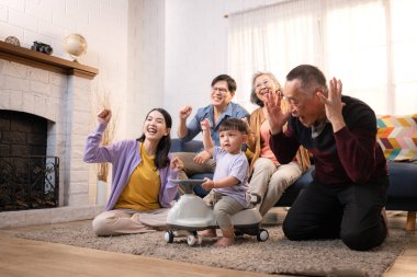 Mutlu çoklu Asyalı bir aile evde keyifle vakit geçiriyor, oyuncak bir arabayla rahat bir oturma odasında gülümsüyor ve gülümsüyor.