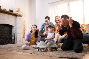 Mutlu çoklu Asyalı bir aile evde keyifle vakit geçiriyor, oyuncak bir arabayla rahat bir oturma odasında gülümsüyor ve gülümsüyor.