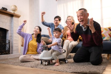 Mutlu çoklu Asyalı bir aile evde keyifle vakit geçiriyor, oyuncak bir arabayla rahat bir oturma odasında gülümsüyor ve gülümsüyor.