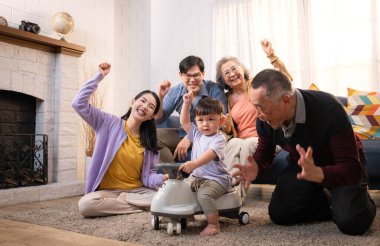 Mutlu çoklu Asyalı bir aile evde keyifle vakit geçiriyor, oyuncak bir arabayla rahat bir oturma odasında gülümsüyor ve gülümsüyor.