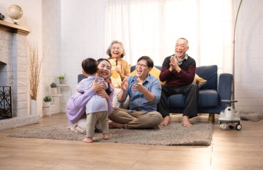Mutlu çoklu Asyalı aile evde birlikte eğleniyor, bir bebekle tezahürat yapıyor ve gülümsüyor.