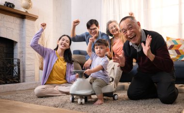 Mutlu çoklu Asyalı bir aile evde keyifle vakit geçiriyor, oyuncak bir arabayla rahat bir oturma odasında gülümsüyor ve gülümsüyor.