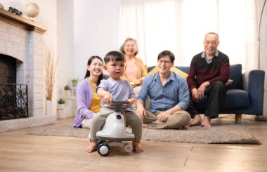 Mutlu çoklu Asyalı bir aile evde keyifle vakit geçiriyor, oyuncak bir arabayla rahat bir oturma odasında gülümsüyor ve gülümsüyor.