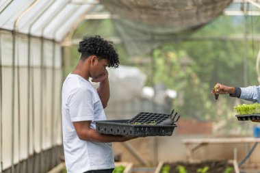 Bir serada filizlenen filizlenmeyi tartışan ve elinde tepsiler dolusu filizle sürdürülebilir tarım yapmayı öğrenen iki genç insan.