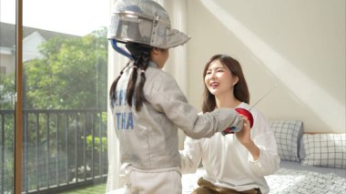 Eskrim kıyafeti giymiş bir kız, yaklaşan müsabaka gününe hazırlanmak için eskrim antrenmanından önce annesiyle spor malzemeleri hazırlıyor.