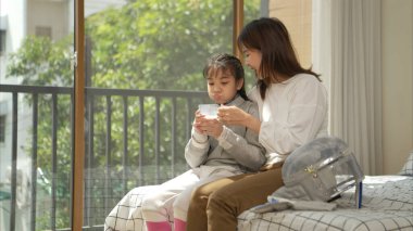 Eskrim kıyafeti giymiş bir kız, anneleriyle birlikte yaklaşan müsabaka gününe hazırlanmak için eskrim antrenmanından önce süt ve spor malzemeleri hazırlıyor.