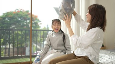 Eskrim kıyafeti giymiş bir kız, yaklaşan müsabaka gününe hazırlanmak için eskrim antrenmanından önce annesiyle spor malzemeleri hazırlıyor.