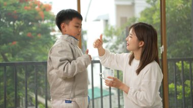 Eskrim kıyafeti giymiş bir çocuk, yaklaşan müsabaka gününe hazırlanmak için eskrim antrenmanından önce annesiyle spor malzemeleri hazırlıyor.