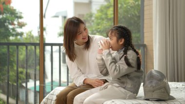 Eskrim kıyafeti giymiş bir kız, anneleriyle birlikte yaklaşan müsabaka gününe hazırlanmak için eskrim antrenmanından önce süt ve spor malzemeleri hazırlıyor.