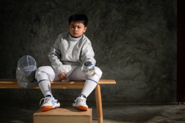 Eskrim kıyafeti giymiş bir çocuk bir bankta oturmuş hazırlık yarışmasına hazırlanıyor.