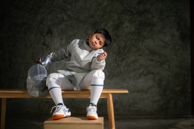 Eskrim kıyafeti giymiş bir çocuk bir bankta oturmuş hazırlık yarışmasına hazırlanıyor.