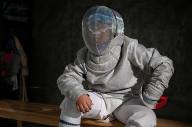 Eskrim kıyafeti giymiş bir çocuk bir bankta oturmuş hazırlık yarışmasına hazırlanıyor.