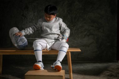 Eskrim kıyafeti giymiş bir çocuk bir bankta oturmuş hazırlık yarışmasına hazırlanıyor.