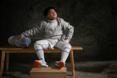 Eskrim kıyafeti giymiş bir çocuk bir bankta oturmuş hazırlık yarışmasına hazırlanıyor.