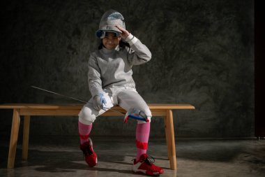 Eskrim kıyafetli bir kız bankta oturuyor, hazırlık yarışmasına hazır.