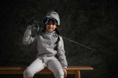 Eskrim kıyafetli bir kız bankta oturuyor, hazırlık yarışmasına hazır.