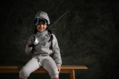 Eskrim kıyafetli bir kız bankta oturuyor, hazırlık yarışmasına hazır.