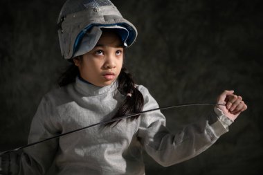 Eskrim kıyafetli bir kız bankta oturuyor, hazırlık yarışmasına hazır.