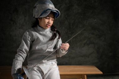 Eskrim kıyafetli bir kız bankta oturuyor, hazırlık yarışmasına hazır.