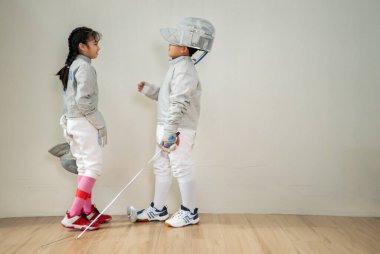 Turnuva gününden önce, eskrim kıyafeti giymiş bir kız ve erkek spor salonunda prova yapıyorlar.