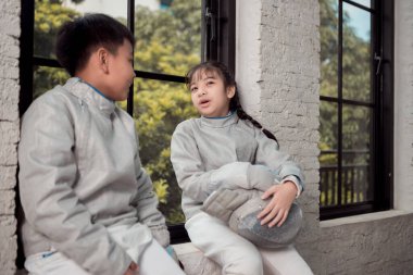 Turnuva gününden önce, eskrim kıyafeti giymiş bir kız ve erkek spor salonunda prova yapıyorlar.