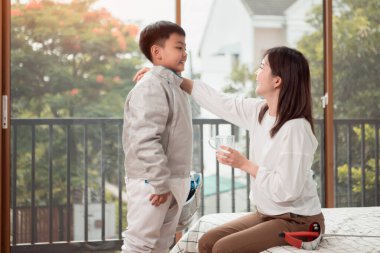 Eskrim kıyafeti giymiş bir çocuk anneleriyle birlikte yaklaşan müsabaka gününe hazırlanmak için eskrim antrenmanından önce yiyecek ve spor malzemeleri hazırlıyor.