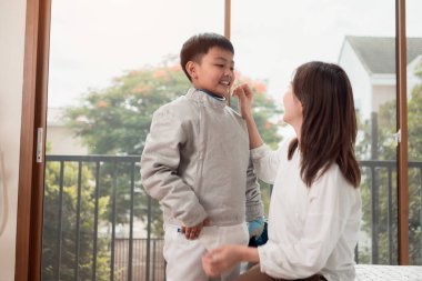 Eskrim kıyafeti giymiş bir çocuk anneleriyle birlikte yaklaşan müsabaka gününe hazırlanmak için eskrim antrenmanından önce yiyecek ve spor malzemeleri hazırlıyor.