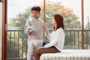 Eskrim kıyafeti giymiş bir çocuk anneleriyle birlikte yaklaşan müsabaka gününe hazırlanmak için eskrim antrenmanından önce yiyecek ve spor malzemeleri hazırlıyor.