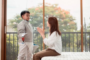 Eskrim kıyafeti giymiş bir çocuk anneleriyle birlikte yaklaşan müsabaka gününe hazırlanmak için eskrim antrenmanından önce yiyecek ve spor malzemeleri hazırlıyor.