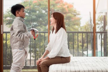 Eskrim kıyafeti giymiş bir çocuk anneleriyle birlikte yaklaşan müsabaka gününe hazırlanmak için eskrim antrenmanından önce yiyecek ve spor malzemeleri hazırlıyor.