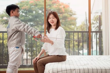 Eskrim kıyafeti giymiş bir çocuk anneleriyle birlikte yaklaşan müsabaka gününe hazırlanmak için eskrim antrenmanından önce yiyecek ve spor malzemeleri hazırlıyor.