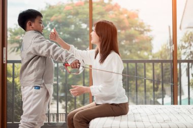 Eskrim kıyafeti giymiş bir çocuk anneleriyle birlikte yaklaşan müsabaka gününe hazırlanmak için eskrim antrenmanından önce yiyecek ve spor malzemeleri hazırlıyor.