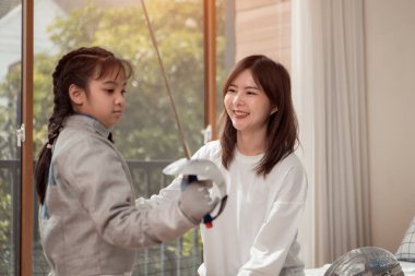 Eskrim kıyafeti giymiş bir kız, anneleriyle birlikte yaklaşan yarışma gününe hazırlık için eskrim antrenmanından önce yiyecek ve spor malzemeleri hazırlıyor.