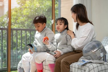 Bir kız ve oğlan, anneleriyle eskrim kıyafetleri içinde yaklaşan müsabakaya hazırlanmak için eskrim antrenmanından önce yiyecek ve spor malzemeleri hazırlıyorlar.